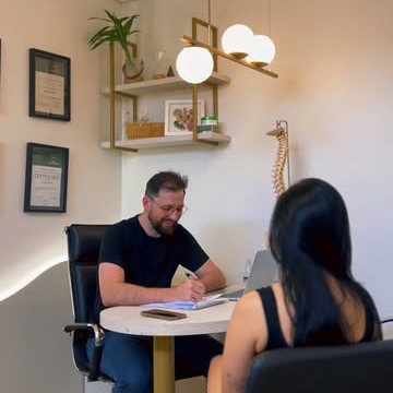Dr. Mateus conversando com uma paciente na mesa do consultório